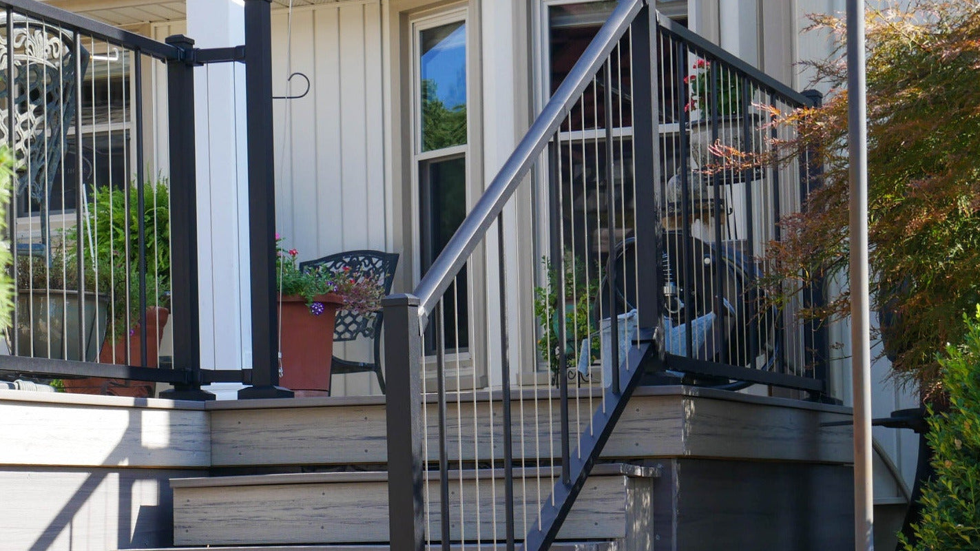 Westbury stainless vertical cable railing on a composite Staircase leading to a house with black railing and greenery around square
