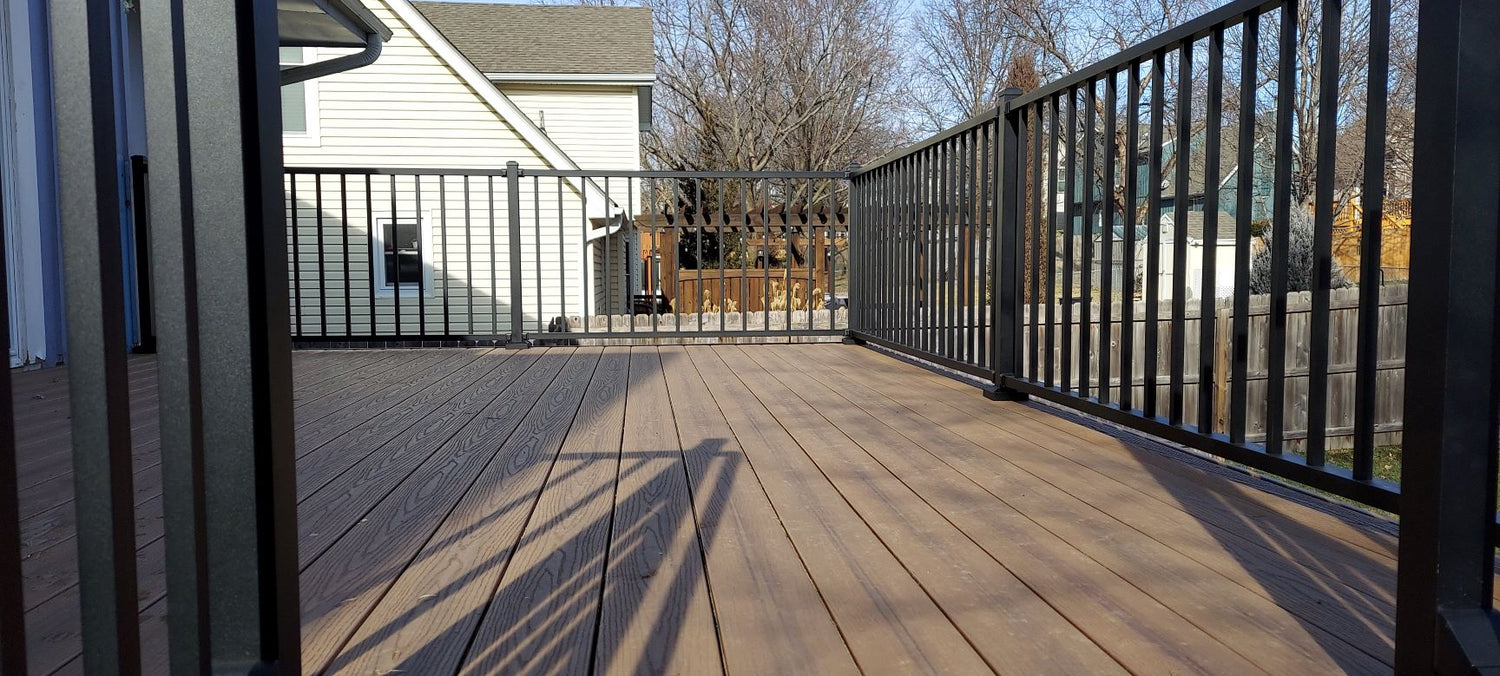 Westbury tuscany deck rail c10 back deck black rail paired with brown composite decking view looking through the top of the stairs and onto the deck with plenty of room. posts and balusters can be seen on the sides of the photo