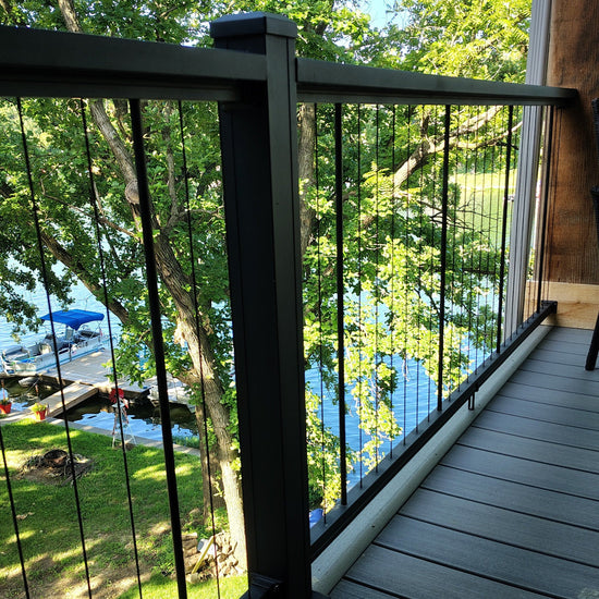 KeyLink Chesapeake Black Vertical Cable Rail with Top Cap(sold separately) to 2.5" fluted posts (sold separately) on a gray composite deck overlooking a lush green backyard with trees and a lake.