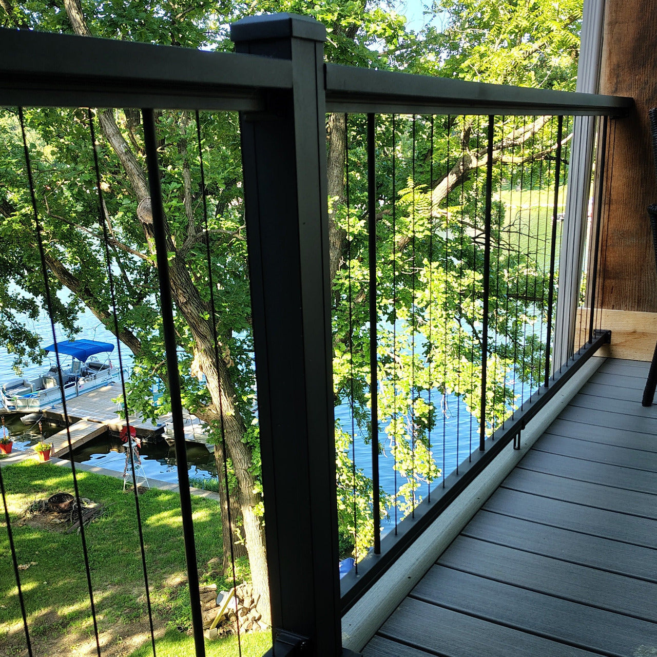 KeyLink Chesapeake Black Vertical Cable Rail with Top Cap(sold separately) to 2.5" fluted posts (sold separately) on a gray composite deck overlooking a lush green backyard with trees and a lake.