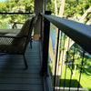 KeyLink Black Cable Vertical Deck Rail  Kits on a dark gray composite deck with outdoor furniture, including a wicker armchair with a beige cushion, a matching coffee table, and a chaise lounge, overlooking a green lawn and trees from a balcony.