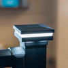 A close-up of a fine texture black westbury magena star lighted outdoor post cap light fixture mounted on a black post, with the light turned on and a warm beige background.