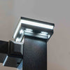 Close-up of a modern black LED light fixture mounted on a wall, with the top panel illuminated and multiple light elements visible against a plain light background.