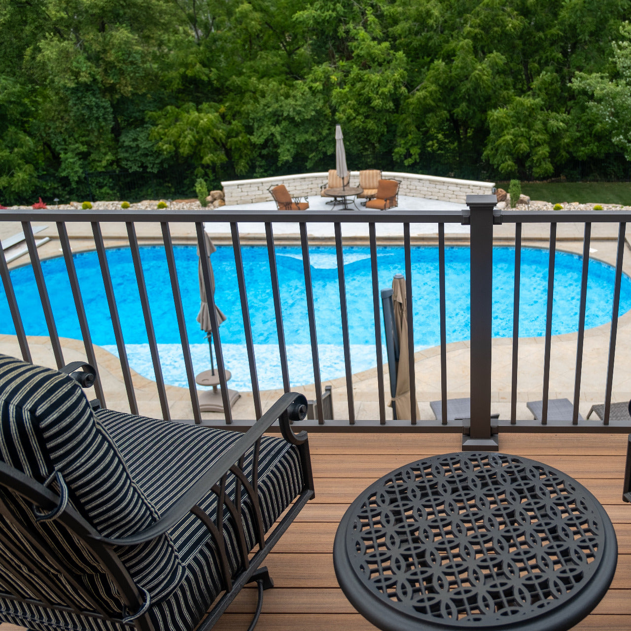 Outdoor deck with pool, chairs, and table, surrounded by greenery with aluminum deck rail and composite decking Square
