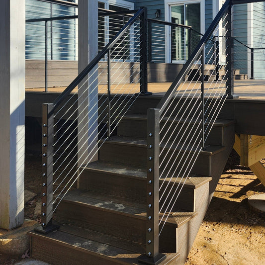 Feeney DesignRailKits Stair Rail Outdoor staircase with black metal 250 stair rail kits and a wooden deck platform attached to a blue house, shown in a backyard setting with bare trees and dirt ground.