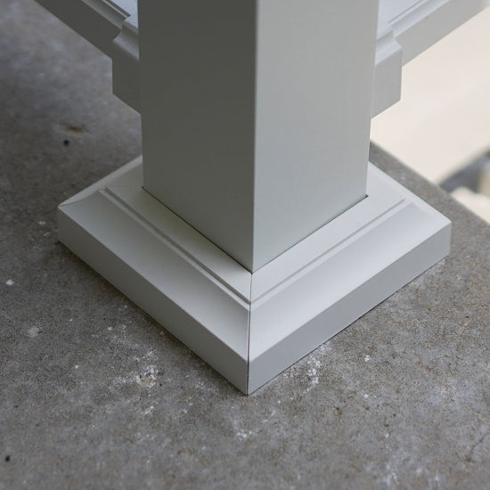 Close-up of a white powder-coated aluminum DekPro Prestige Post Base cover/skirt/flair, shown installed on a gray concrete surface.