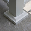 Close-up of a white powder-coated aluminum DekPro Prestige Post Base cover/skirt/flair, shown installed on a gray concrete surface.
