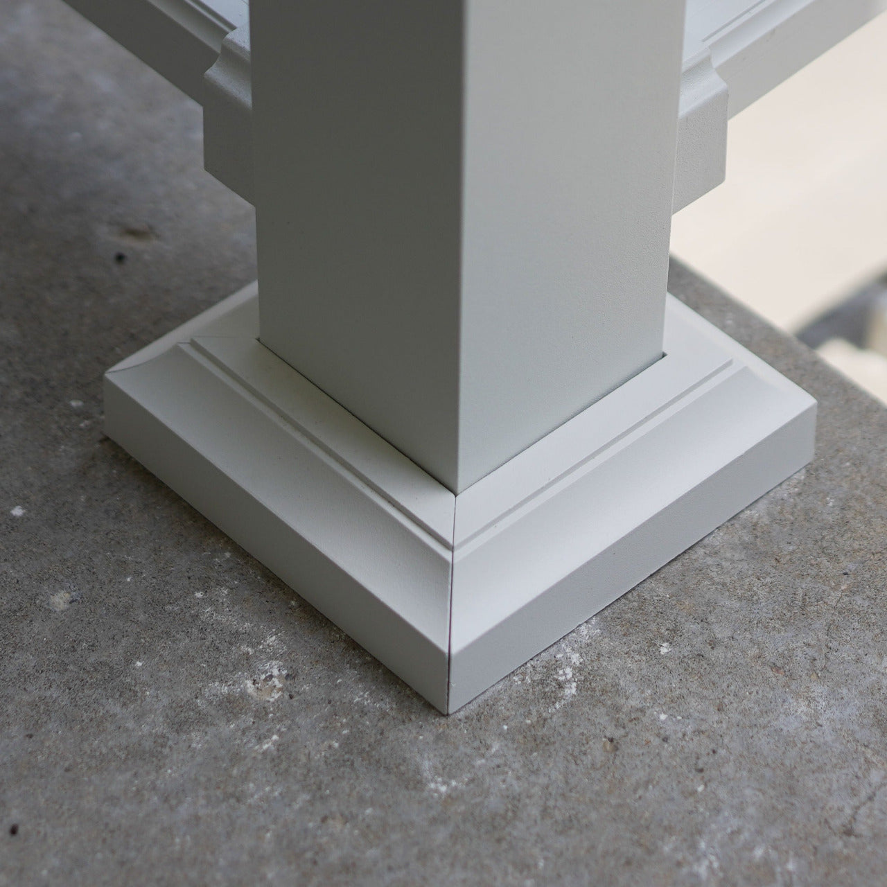 Close-up of a white powder-coated aluminum DekPro Prestige Post Base cover/skirt/flair, shown installed on a gray concrete surface.