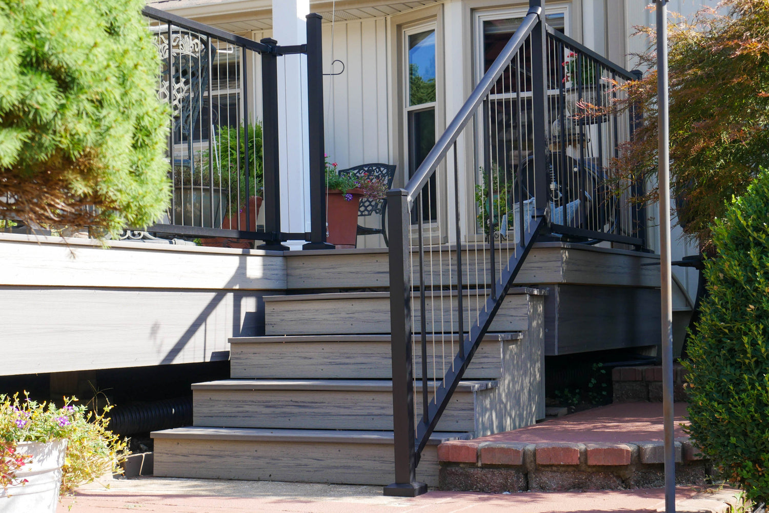 Westbury stainless vertical cable railing on a composite Staircase leading to a house with black railing and greenery around square