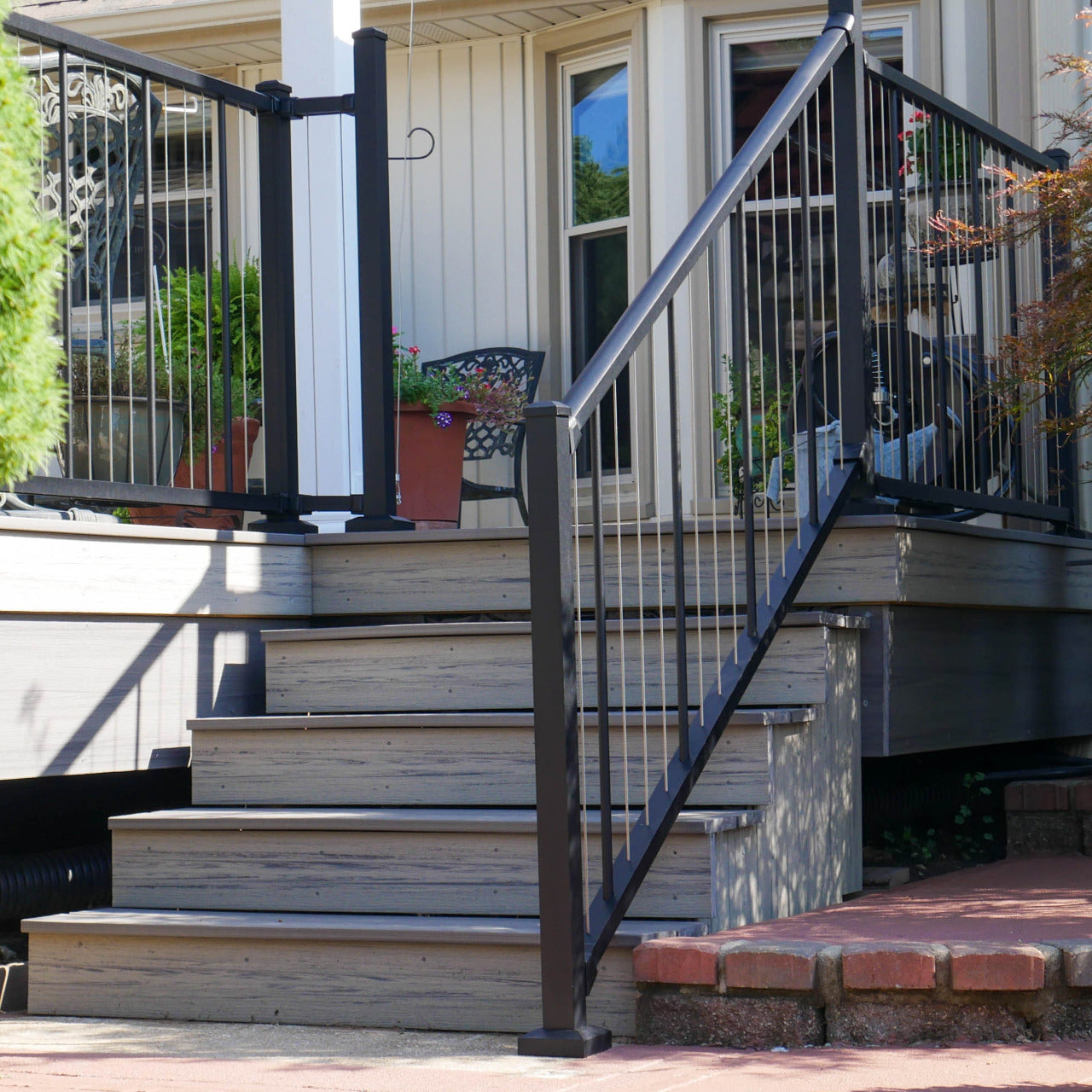Westbury stainless vertical cable railing on a composite Staircase leading to a house with black railing and greenery around square