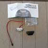 Outdoor LED lighting system component KeyLink Post Accent Light for Posts and Stairs laid out on a porch deck panel background, including a white printed instruction sheet, a red-and-black wire with a small white component, a black cap, and a clear plastic bag of small metal parts.