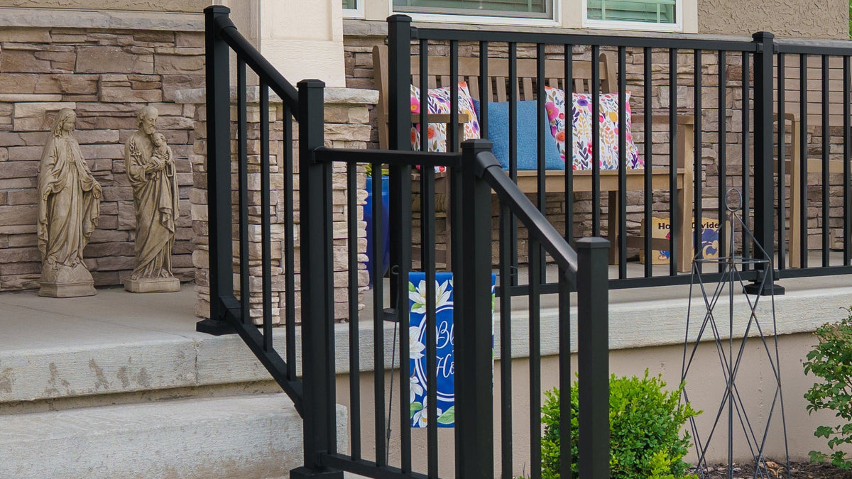 Westbury Tuscany C10 Stair and Level Rail with 2inch Black metal posts on a front porch installed on concrete steps leading to a house porch, shown in a landscaped outdoor setting.