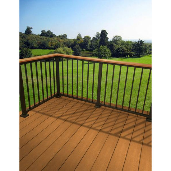 Westbury Drink rail with deck board on a cedar toned deck, aluminum westbury railing infront of an open grassy area and trees in the distance